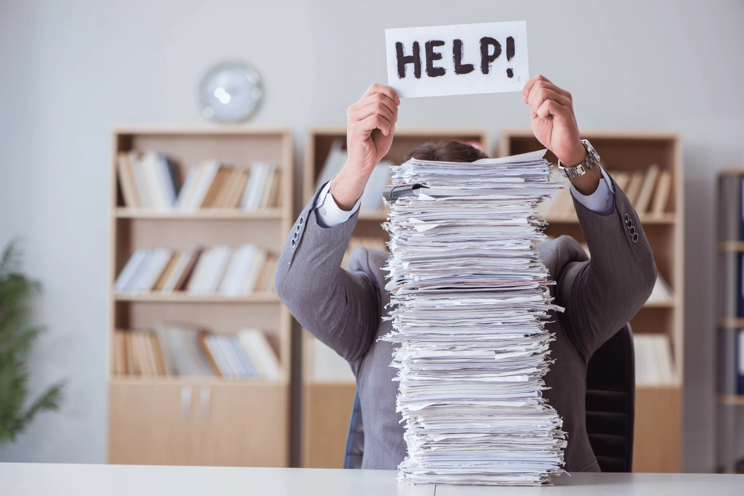 A local government worker covered by a stack of papers holds a help sign up above his head.